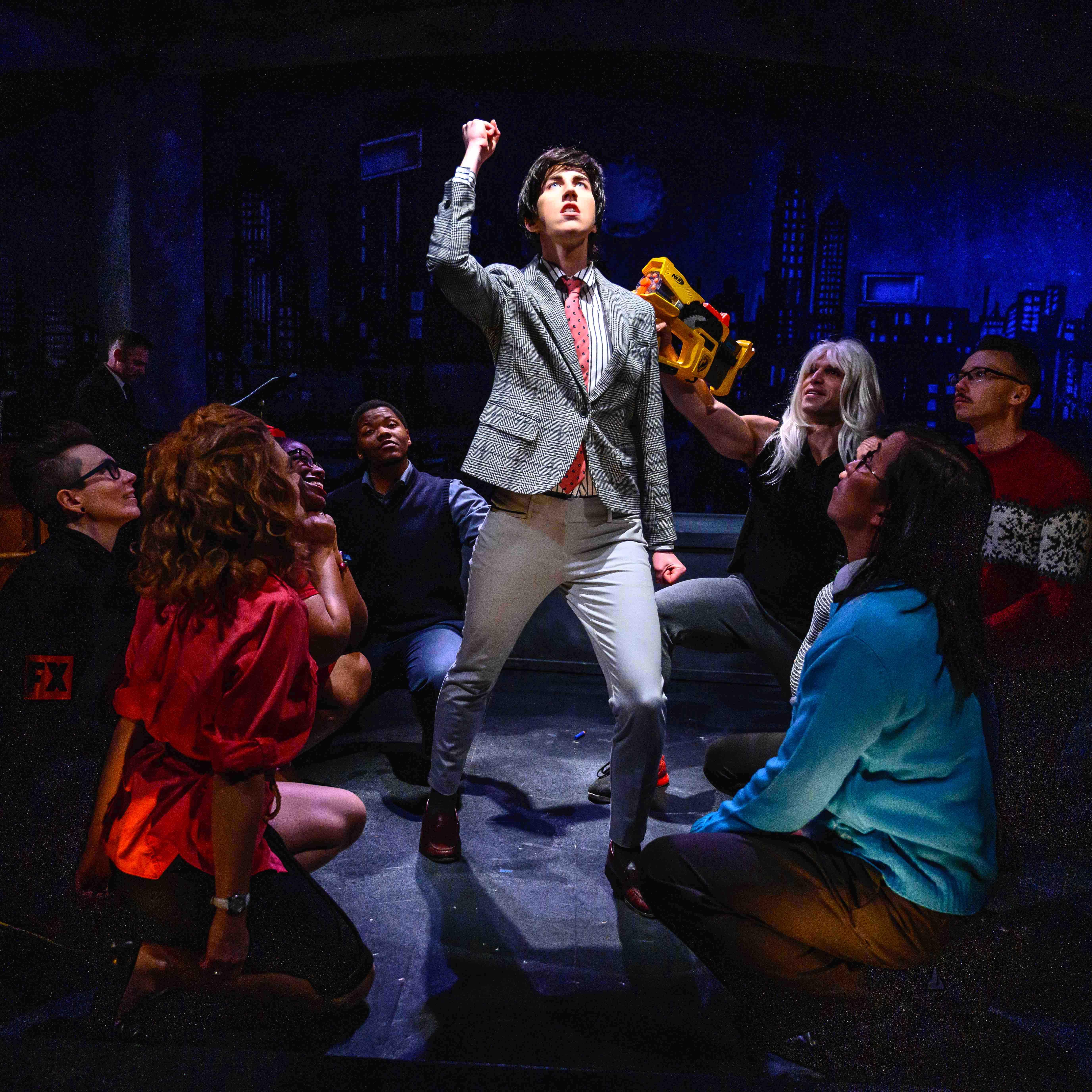 Kat as Ellis stands triumphantly under a spotlight, surrounded by actors on the ground looking up